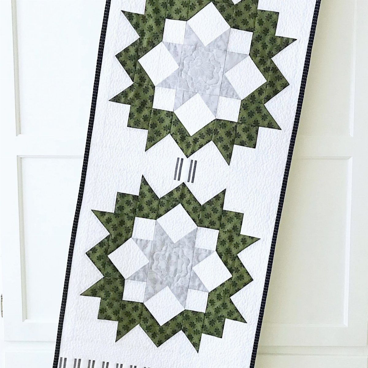 Quilted table runner with two green and white Nordic star patterns on white fabric