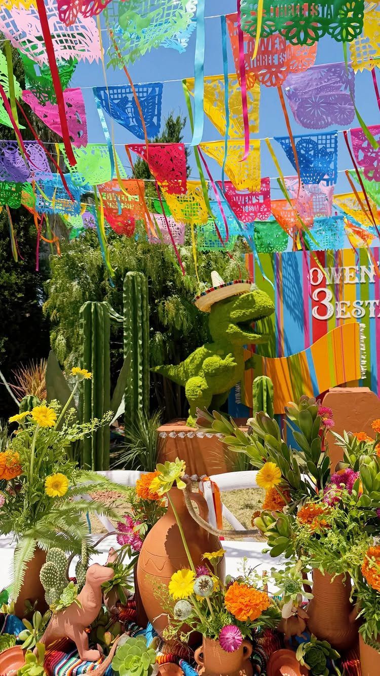 Festive outdoor party table with colorful papel picado banners and dinosaur decorations.