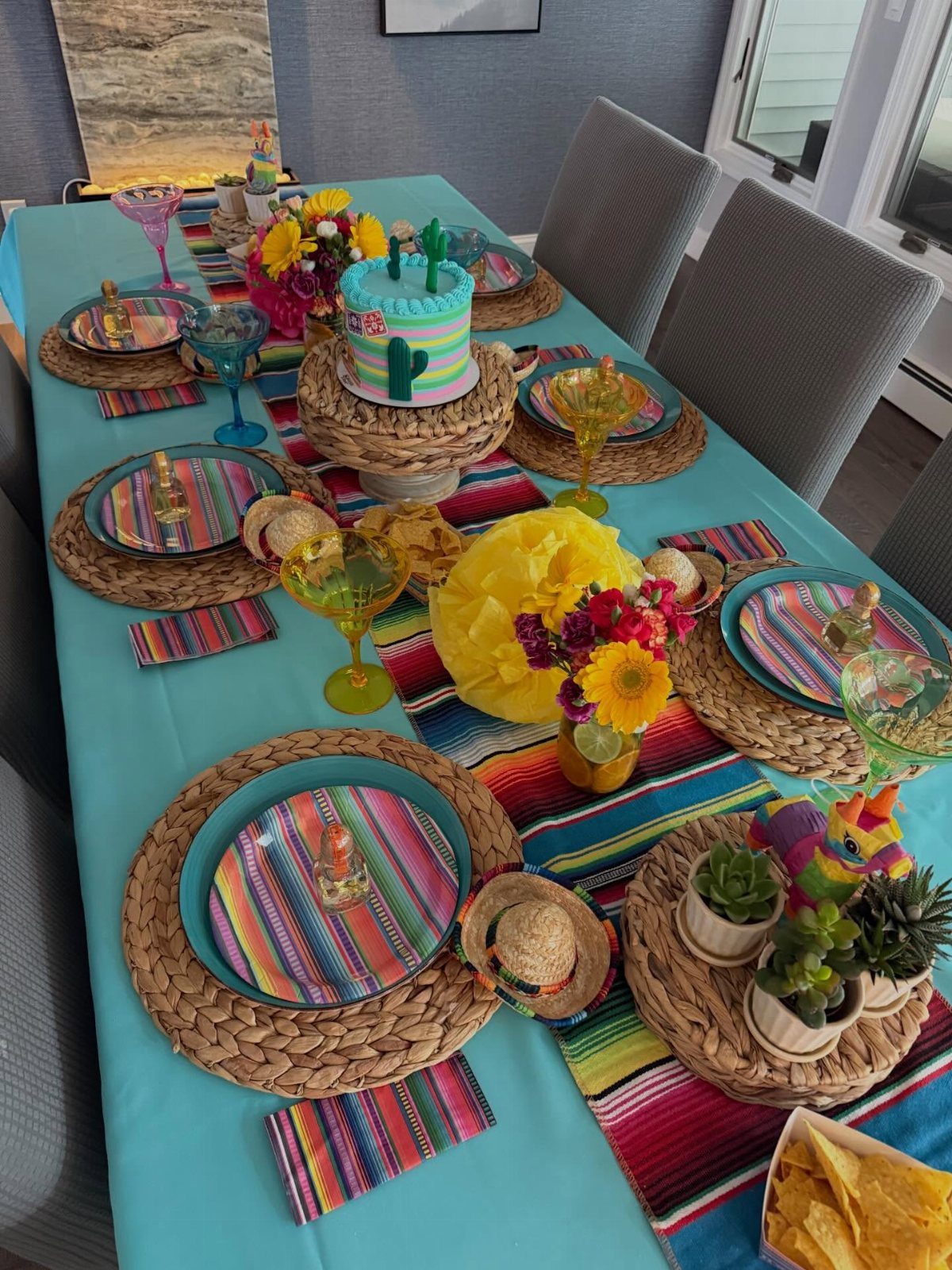 Festive table setting with turquoise tablecloth, striped runner, and colorful napkins.