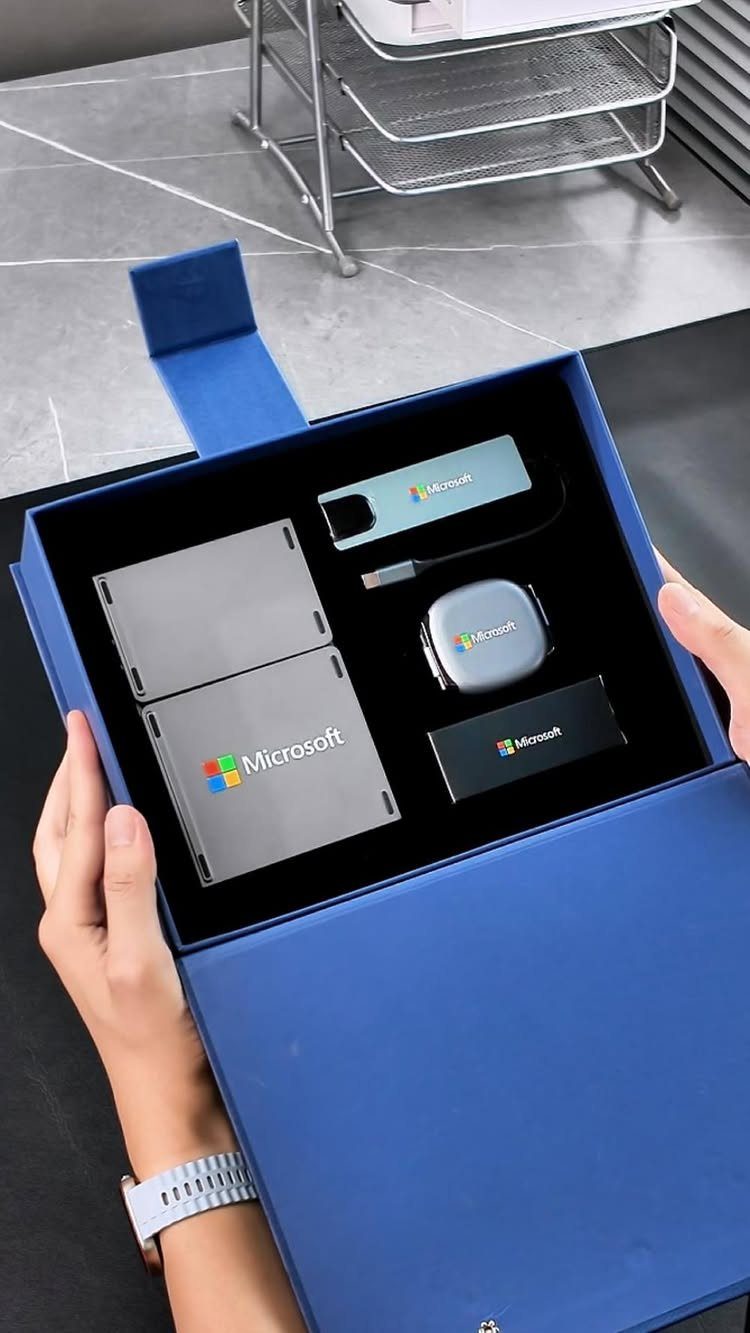 Blue gift box with branded Microsoft tech accessories held by two hands.