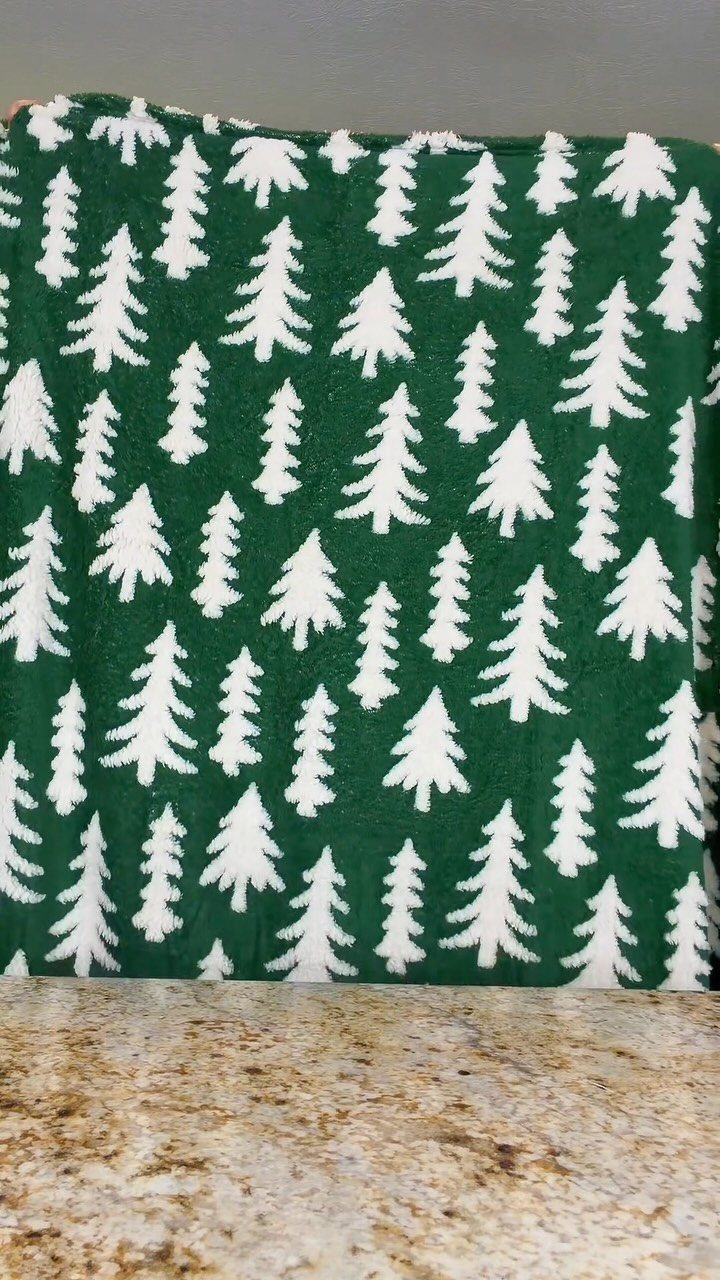 Green plush blanket with white evergreen tree patterns on a beige countertop