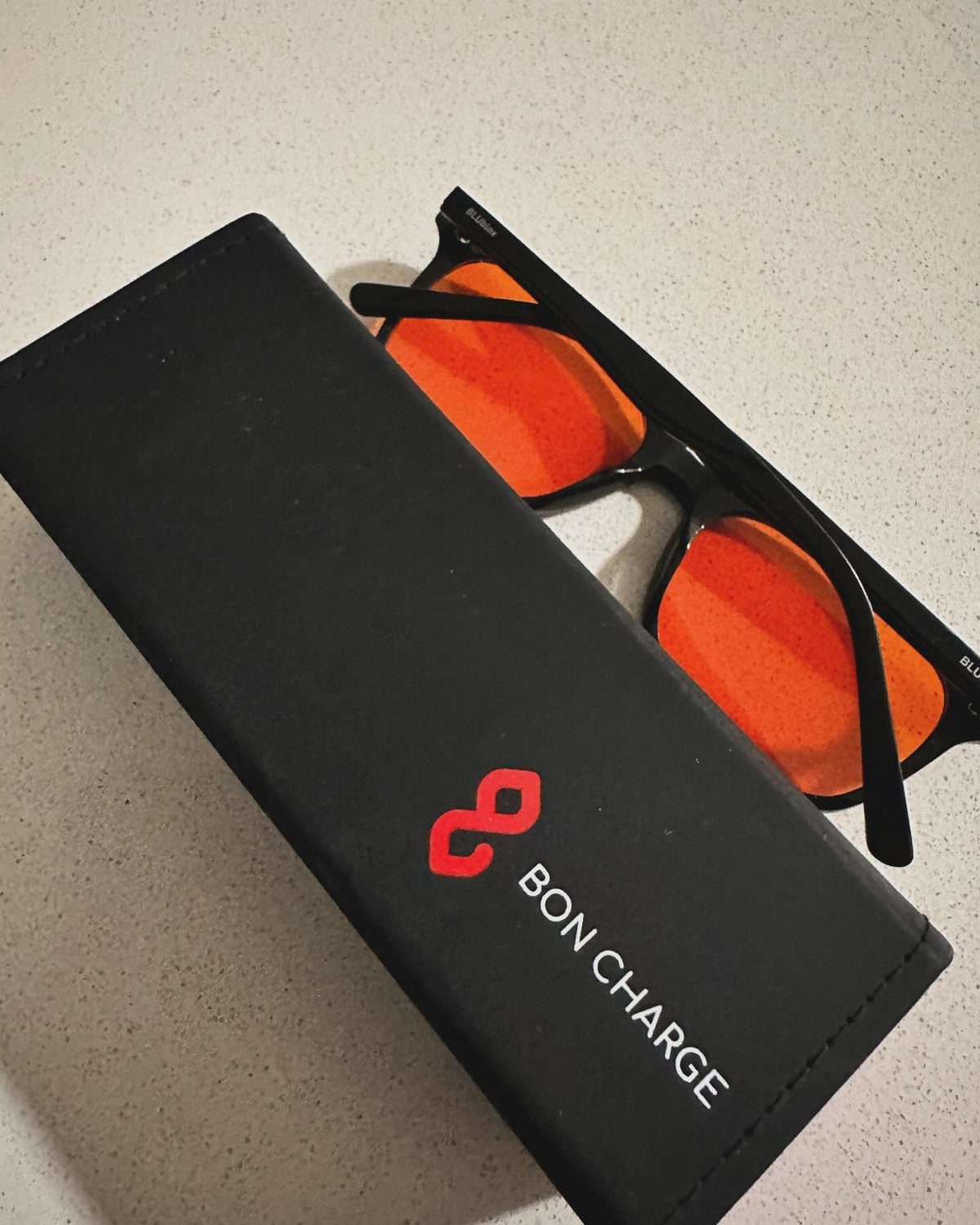 Black-framed blue light glasses with orange lenses and a branded black case.