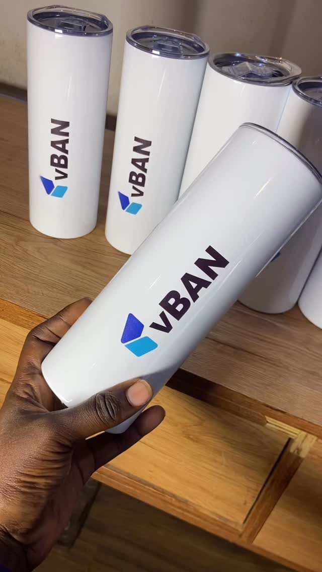 White insulated tumblers with VBAN logo held by a hand on wooden table