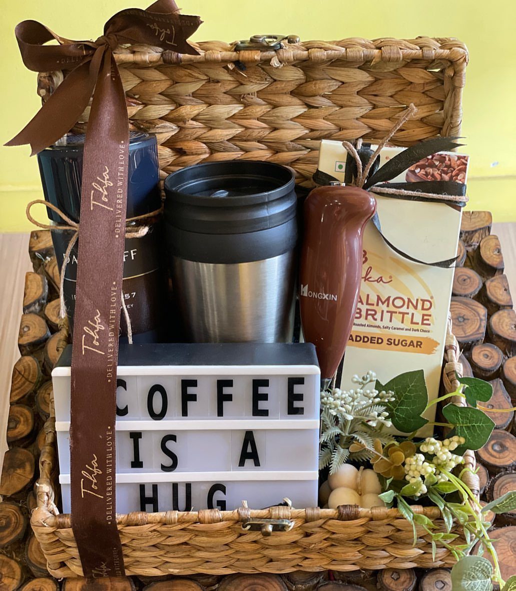 Coffee gift basket with travel mugs, almond brittle, frother, and a coffee lightbox.