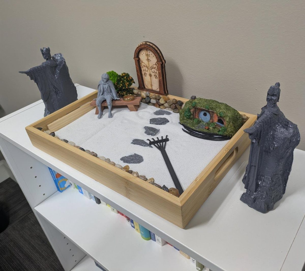 Miniature zen garden with white sand, raked patterns, and small decorative figures.