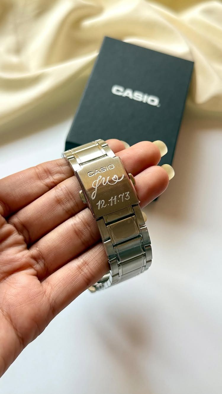 Silver Casio watch band with custom name and date engraving held in hand.
