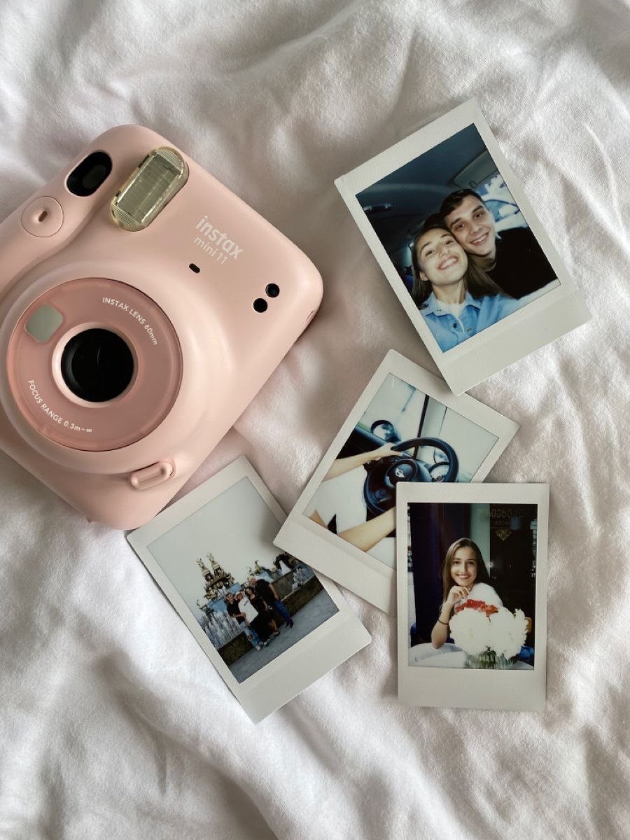Pink Fujifilm Instax Mini camera with several printed instant photos on white fabric.