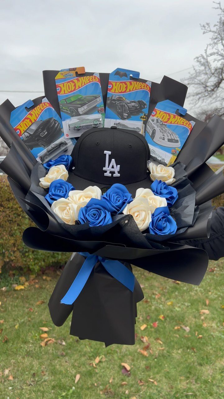 Bouquet of blue and white roses with a baseball cap and toy cars.