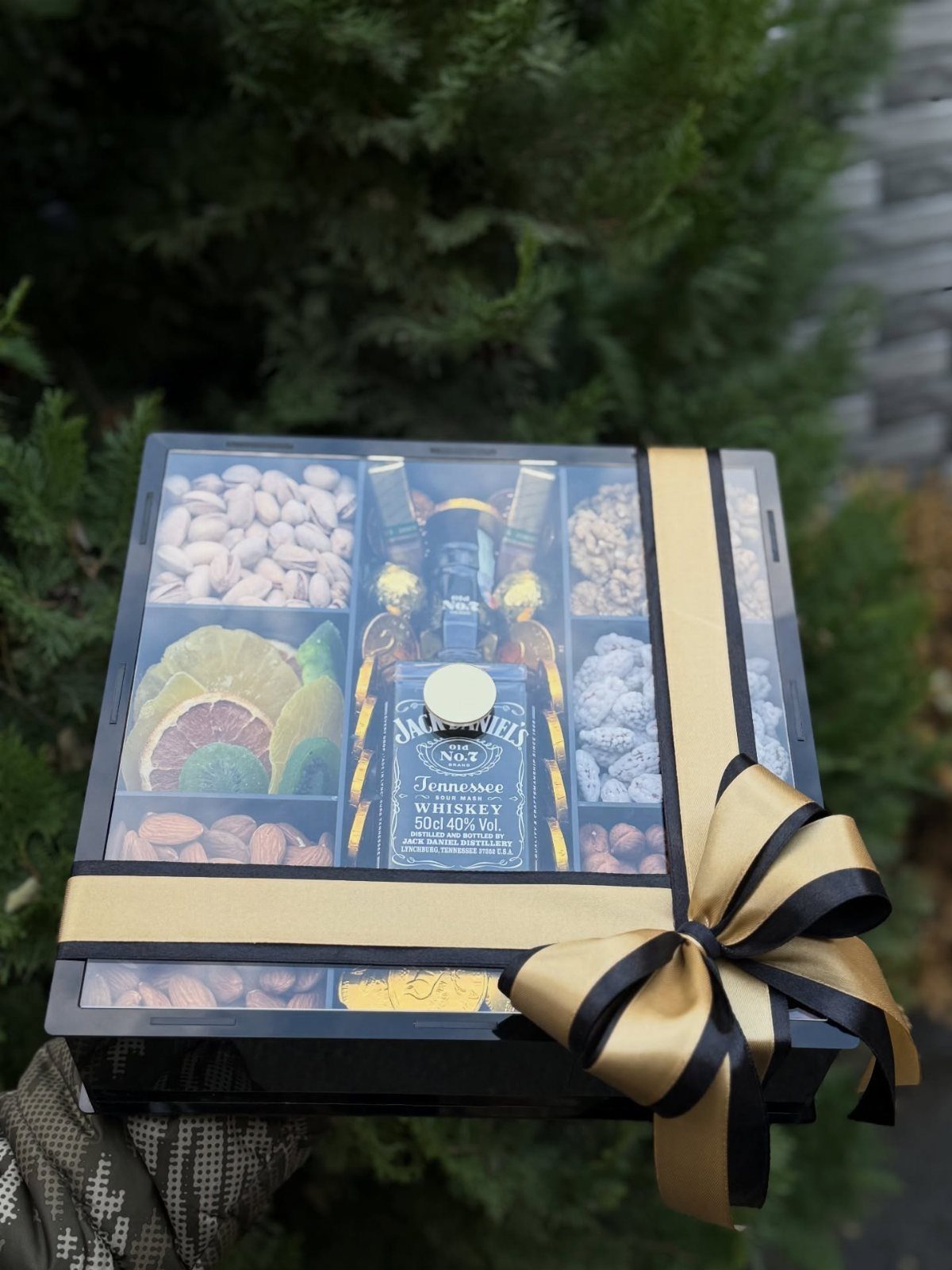 Gift box with whiskey bottle, nuts, and dried fruit tied with gold ribbon.