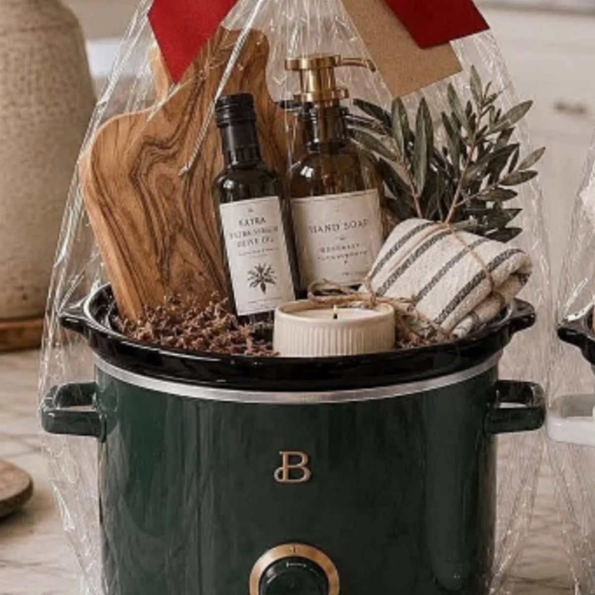 Dark green slow cooker gift basket wrapped in cellophane with gourmet kitchen items.