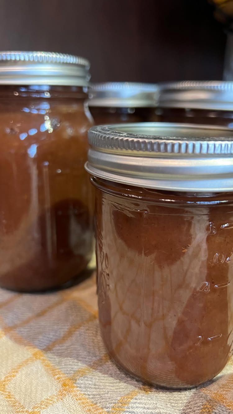 Glass mason jars filled with brown homemade apple butter on checkered cloth