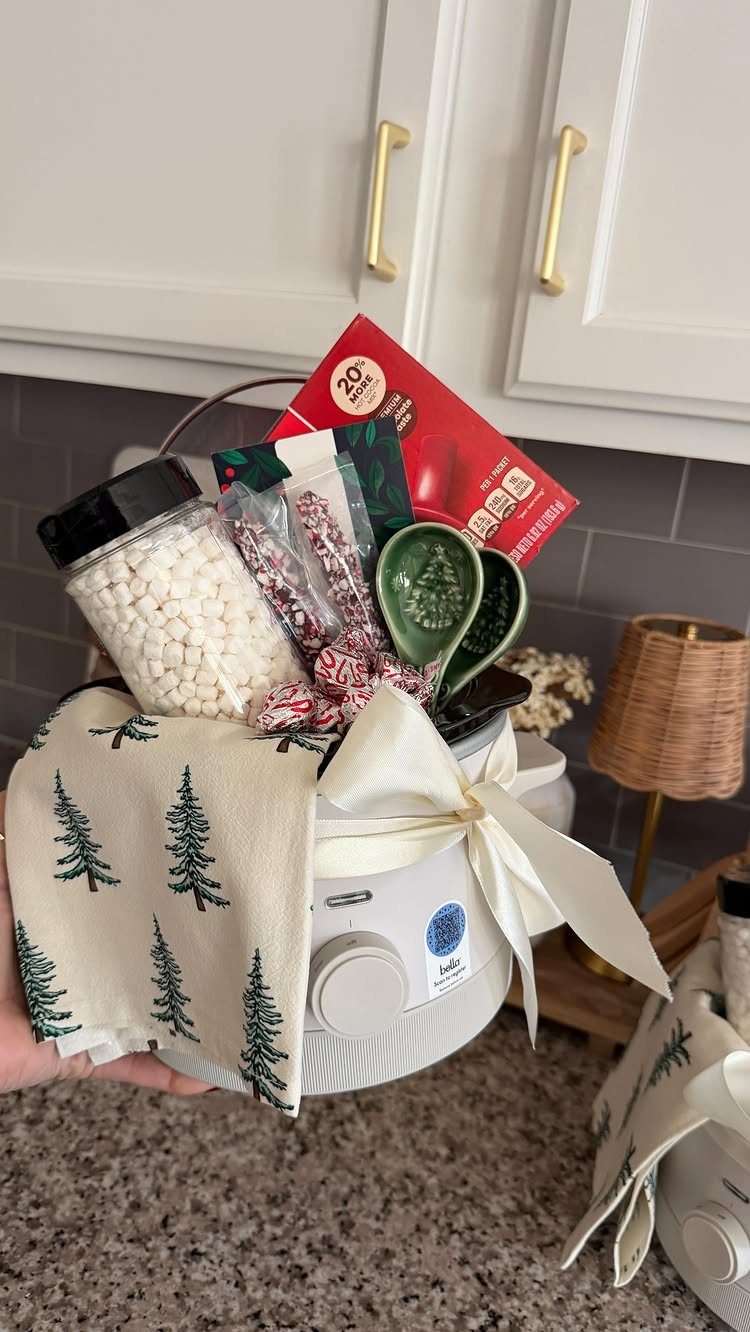 White slow cooker gift basket filled with cocoa, marshmallows, and festive kitchen towels.