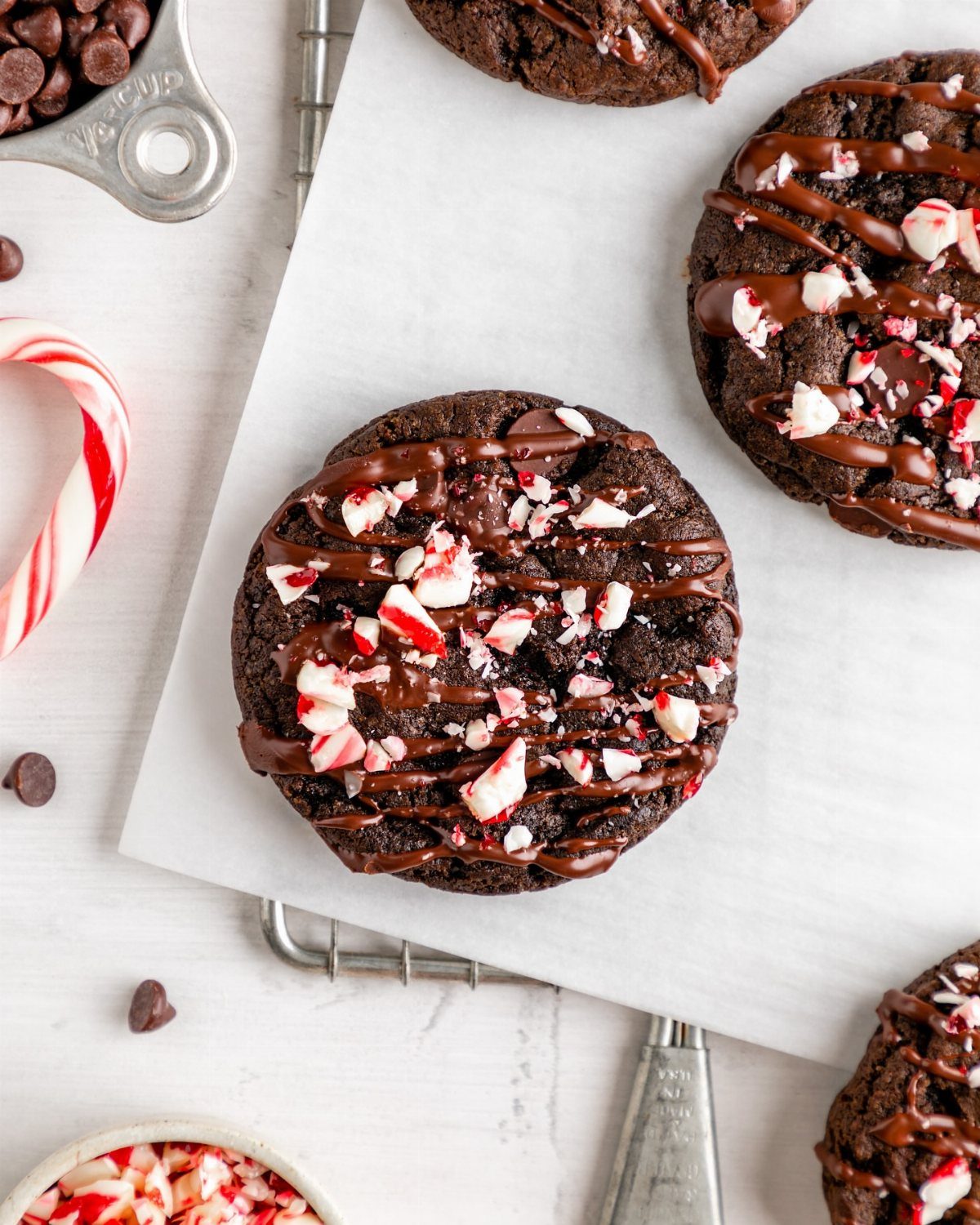 Chocolate peppermint cookies with chocolate drizzle and crushed candy on parchment paper.