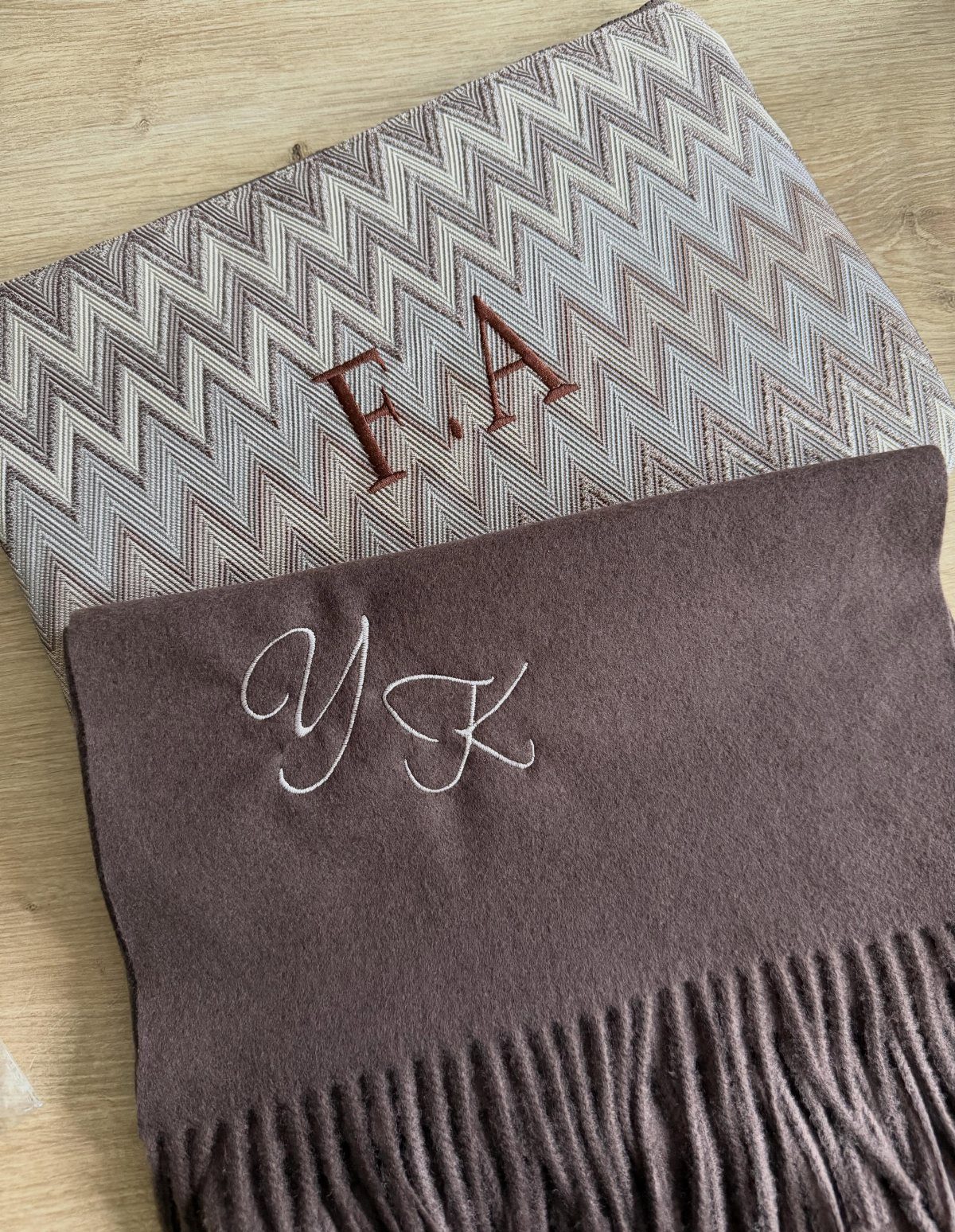 Two monogrammed scarves, one chevron patterned and one solid brown, on wood.