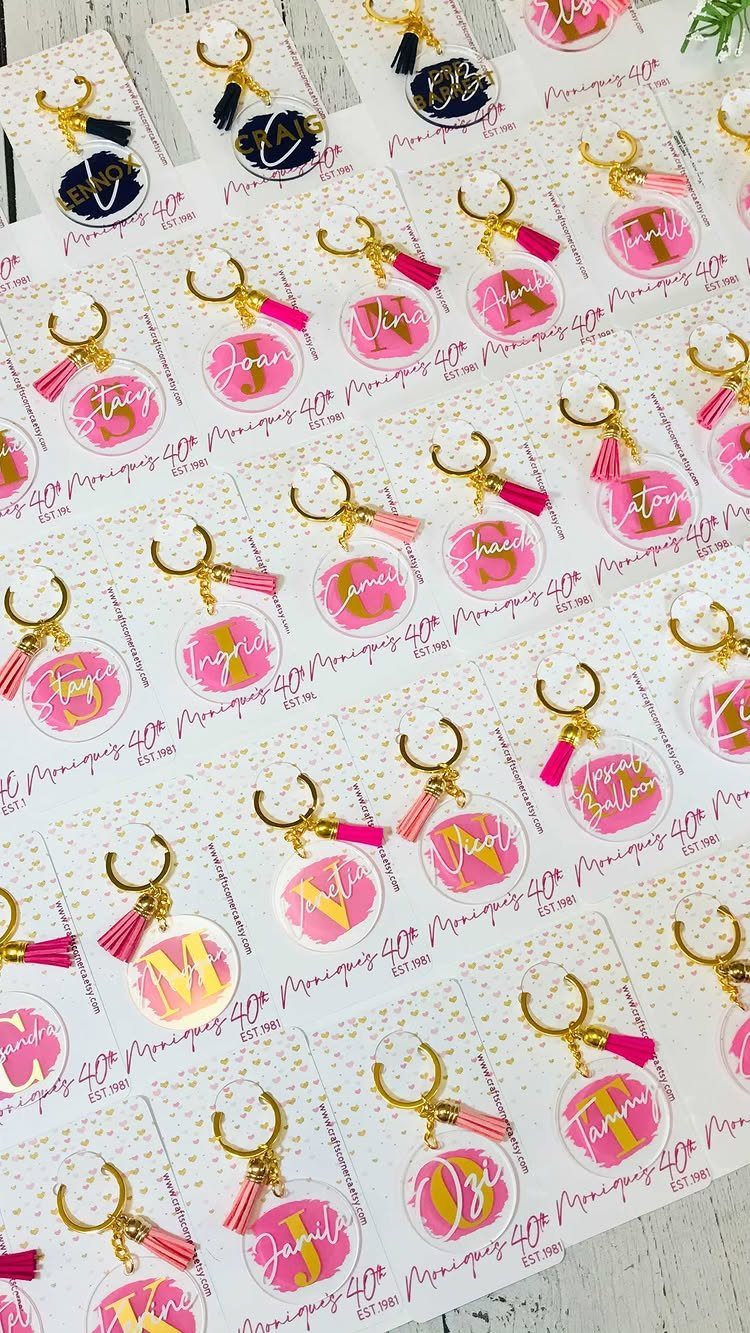 Round acrylic keychains with pink names and gold tassels on decorative cards.