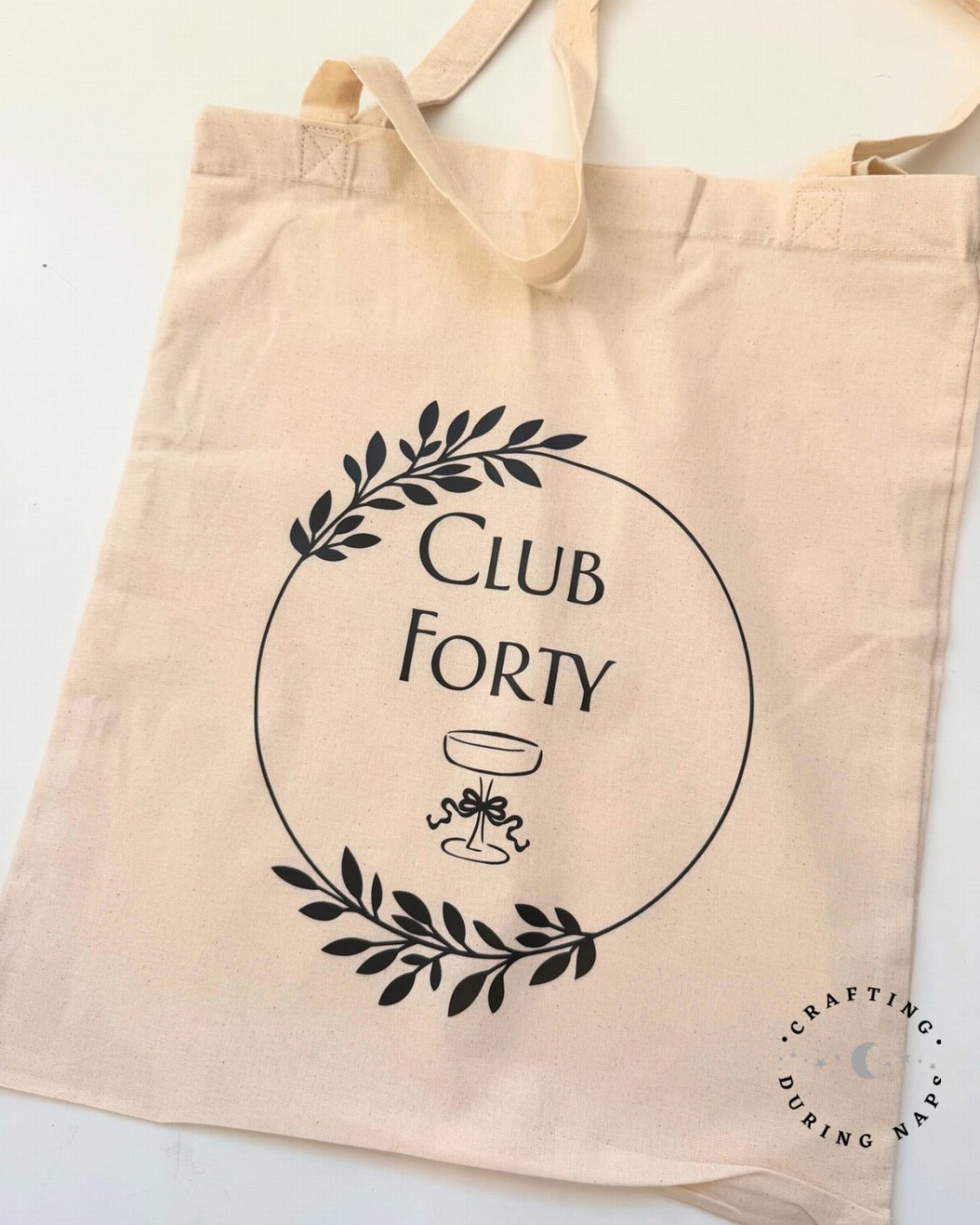 Beige canvas tote bag featuring a black circular logo with text Club Forty.