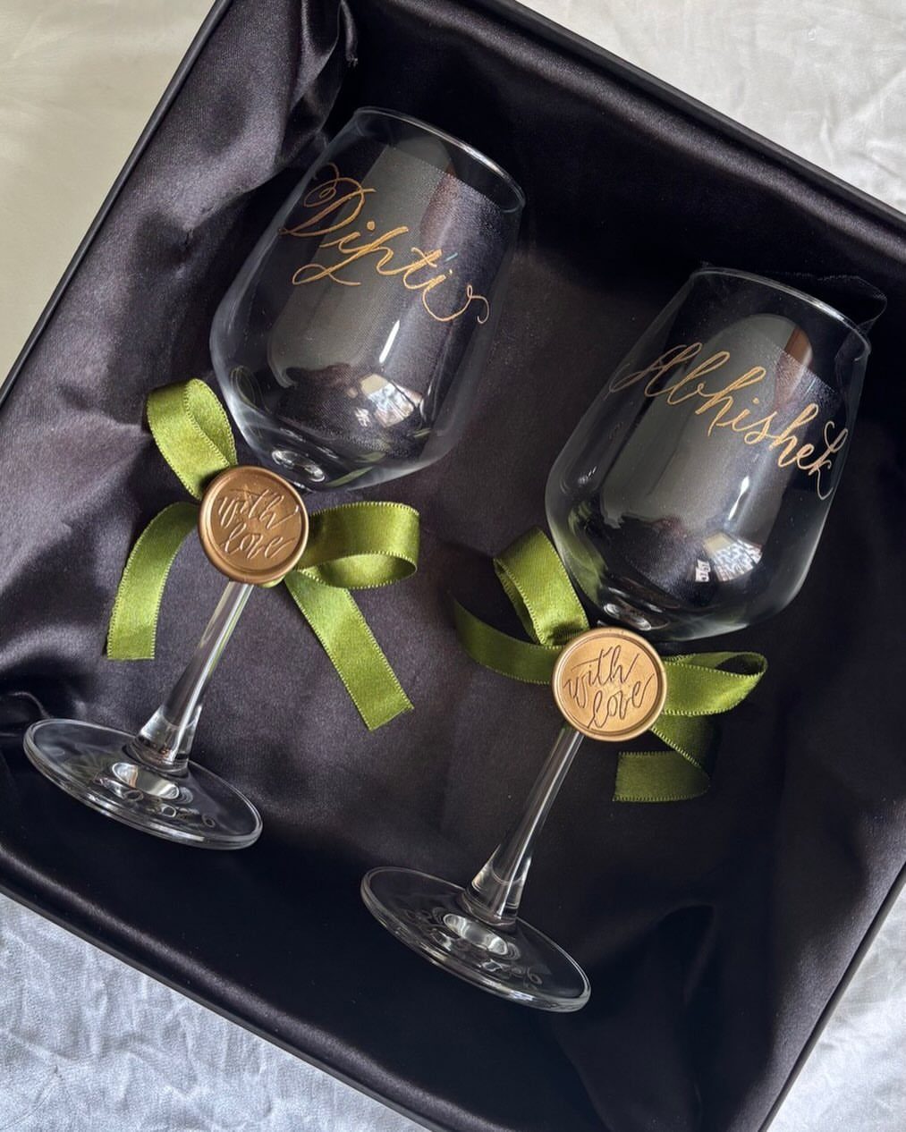 Two personalized wine glasses with gold names in a black satin gift box.