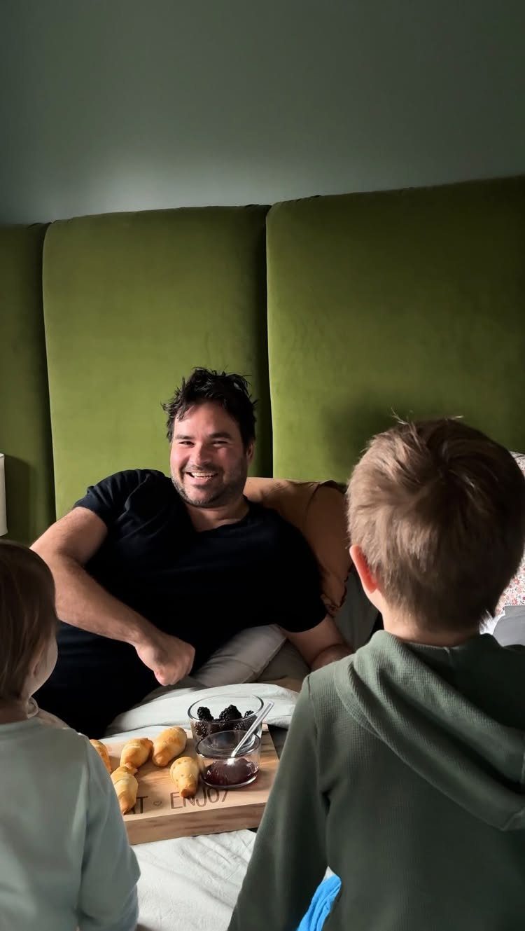 Smiling father in bed receiving breakfast in bed from two young children.