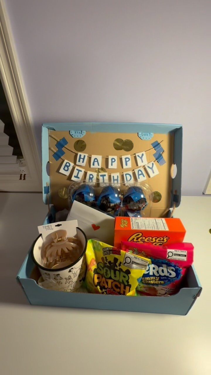Blue birthday gift box filled with assorted candies, a small cake, and banner.