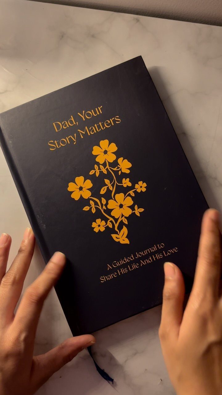Dark blue guided journal for fathers with gold floral design on marble surface