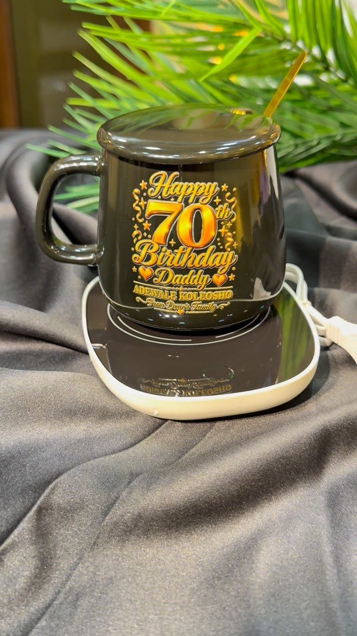Black birthday mug for a 70th birthday sitting on a white warming coaster.