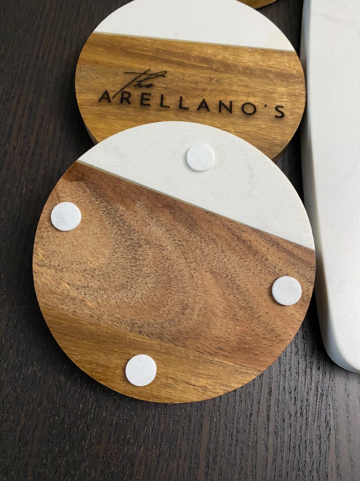 Two circular wood and concrete coasters with one featuring an engraved family name.
