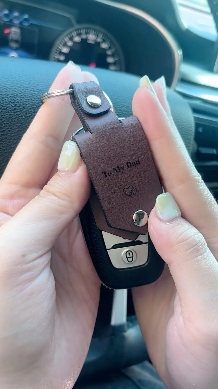 Brown leather keychain engraved with To My Dad held by two hands.