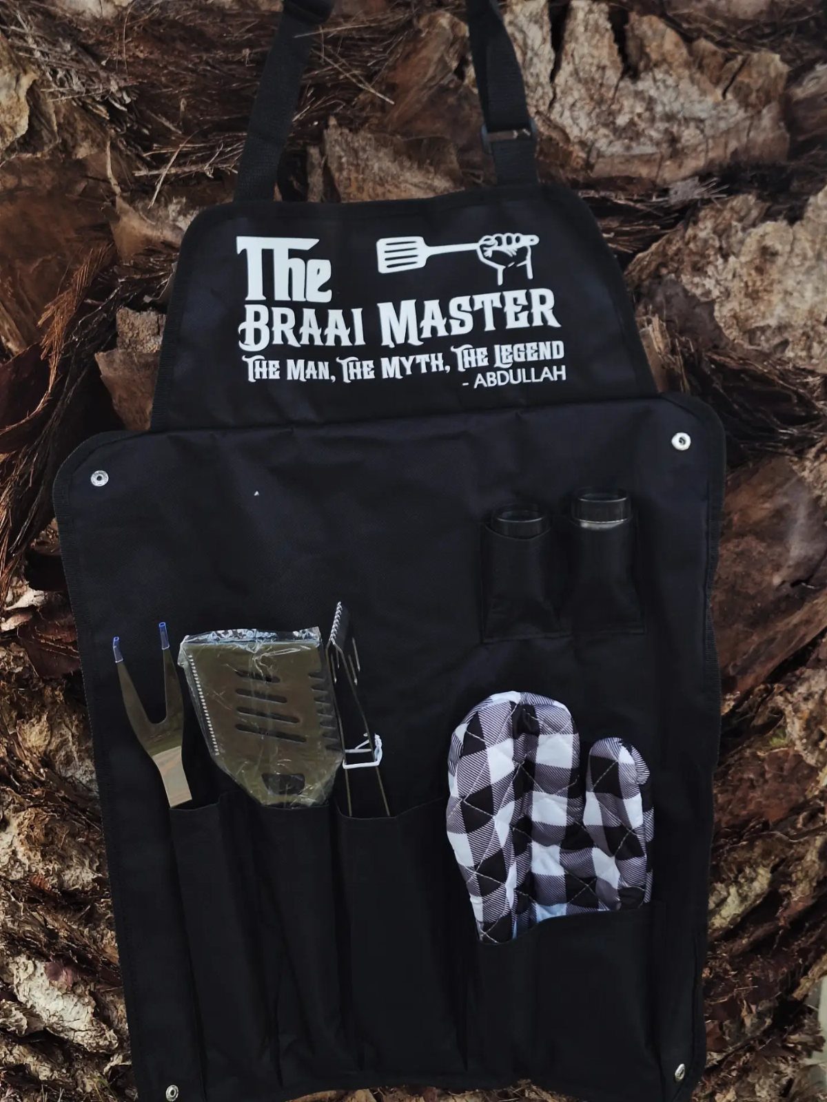 Black personalized grilling apron with tools and oven mitt on a wooden surface