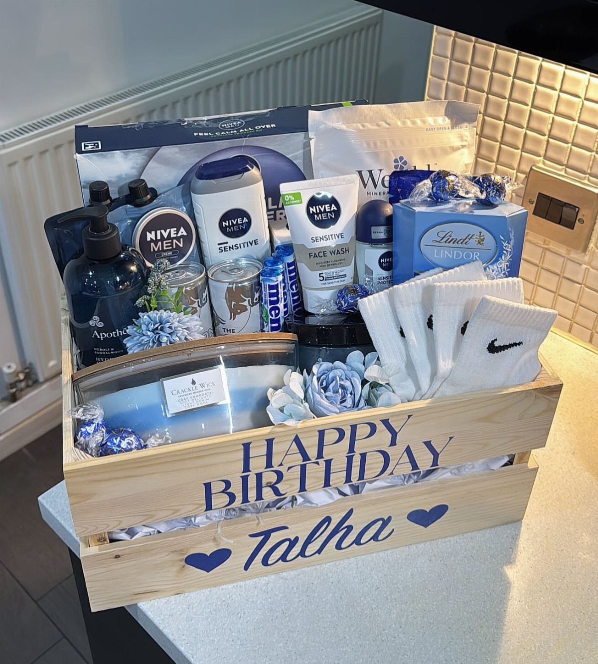 Wooden birthday gift crate filled with men's grooming products, socks, and chocolates.