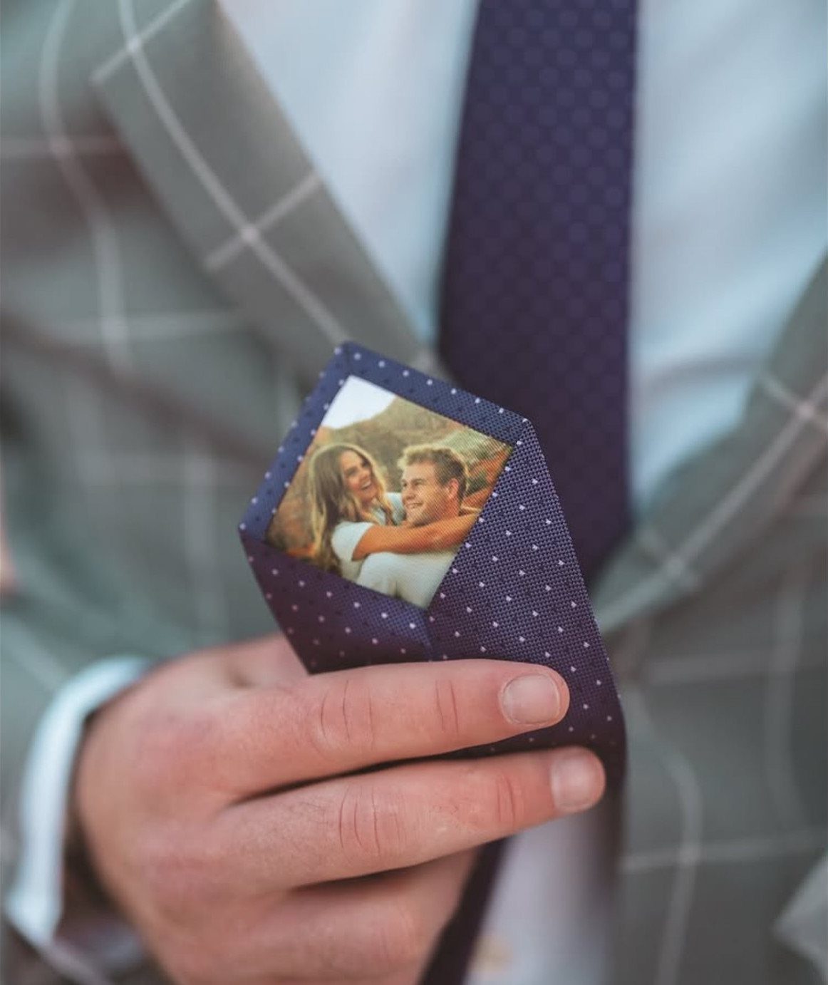Man in a suit holding a blue tie with a hidden photo inside.