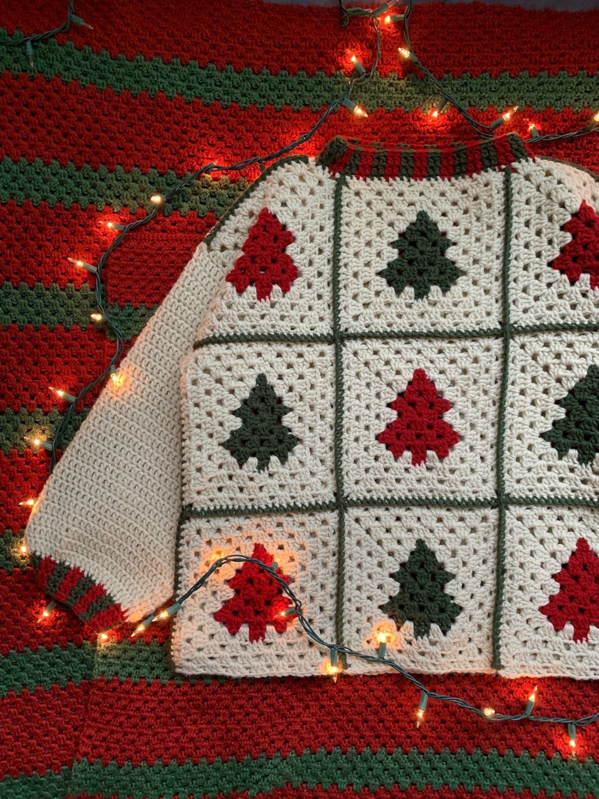 Crocheted white sweater with red and green Christmas trees on a striped blanket