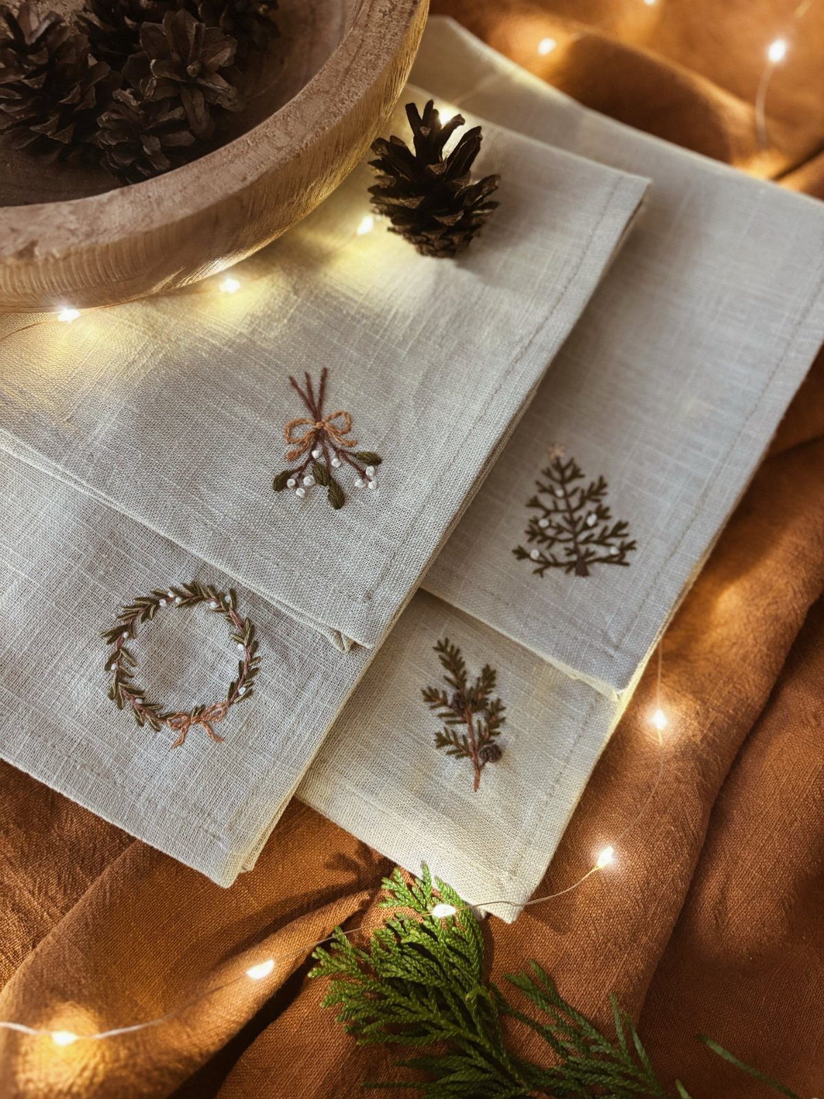 Embroidered beige linen tea towels with festive designs and warm fairy lights.