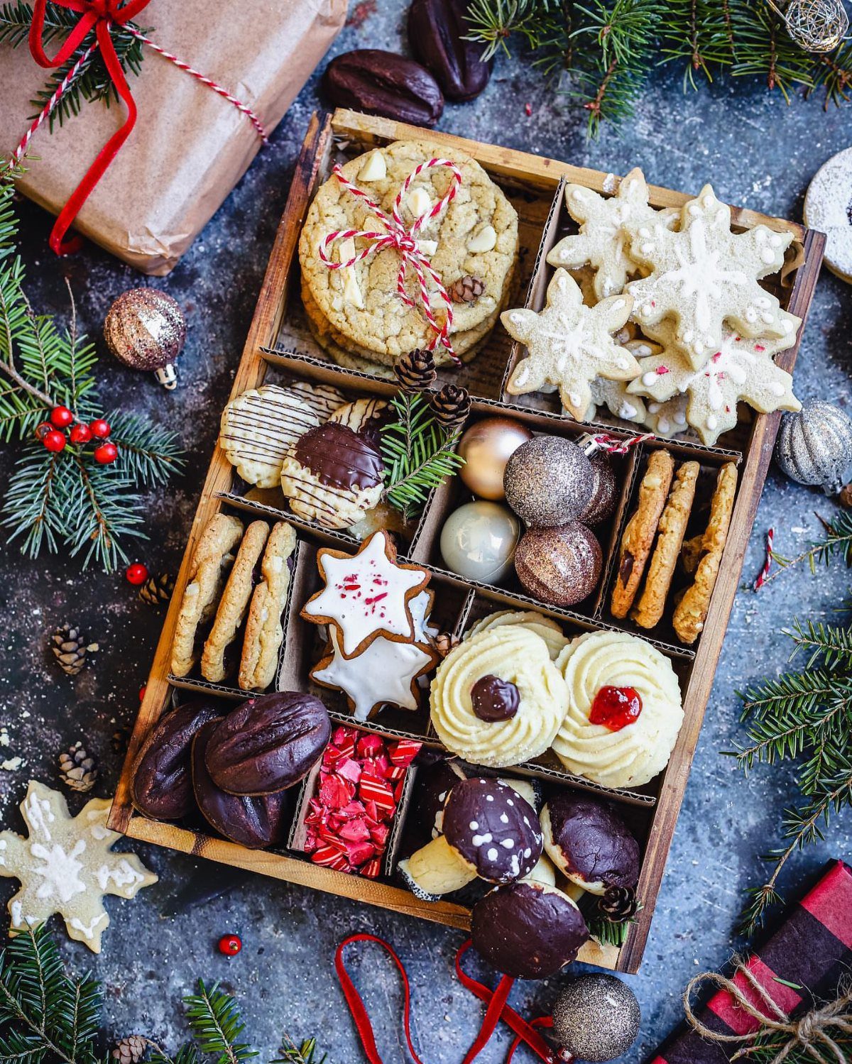 Assorted Christmas cookies in a wooden tray with festive decorations and wrapped gifts.