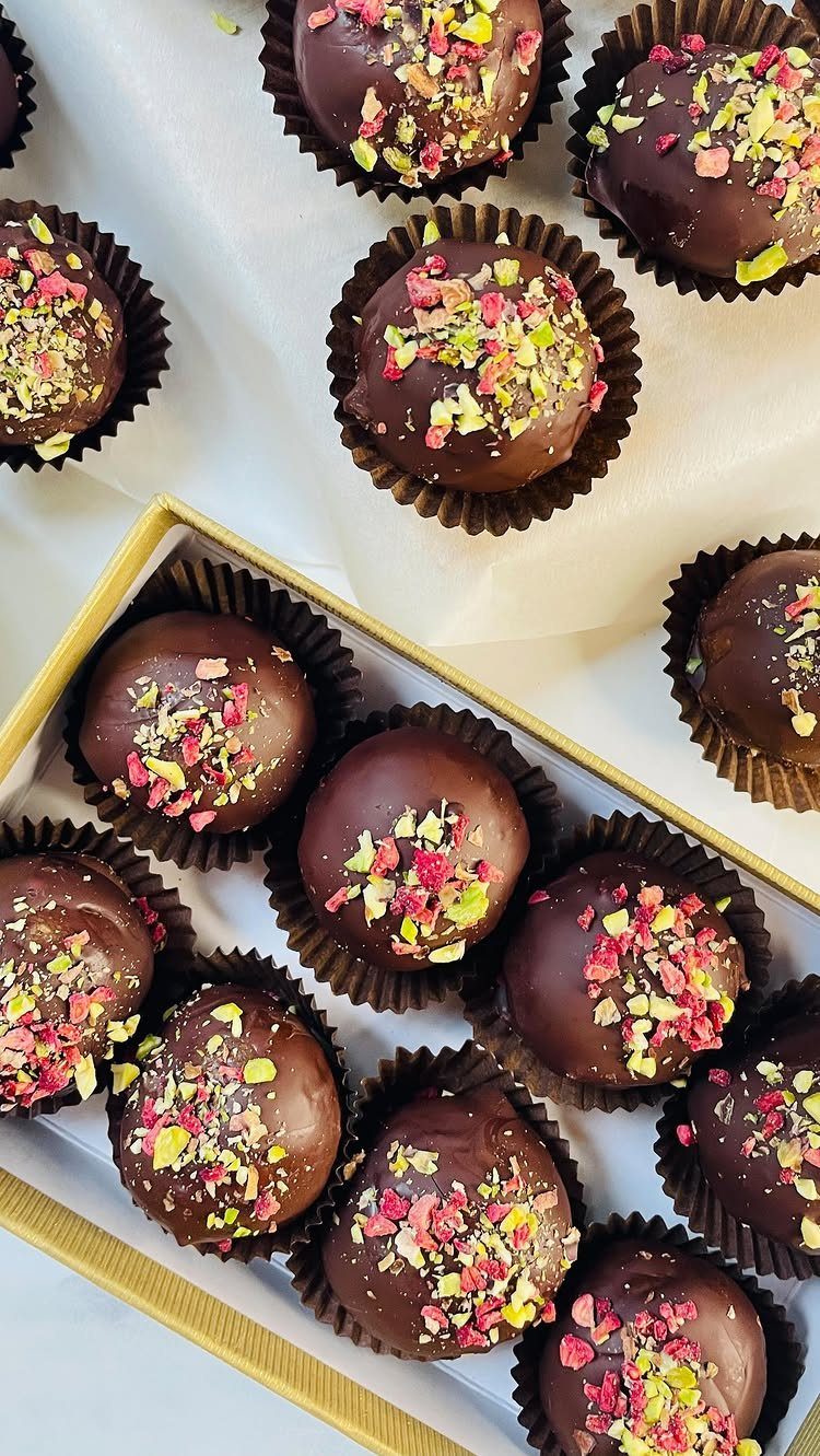 Chocolate truffles with colorful toppings in a gold tin and on parchment paper.