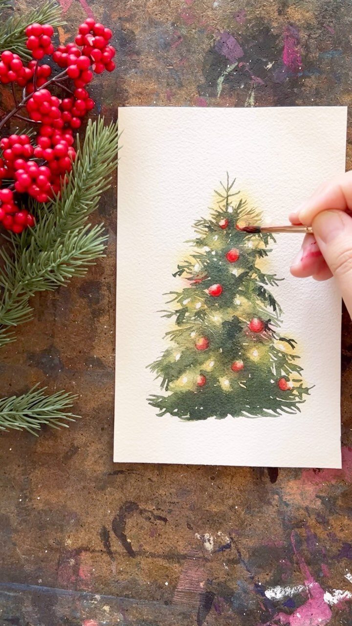 Hand painting a watercolor Christmas tree on white paper with red berries nearby