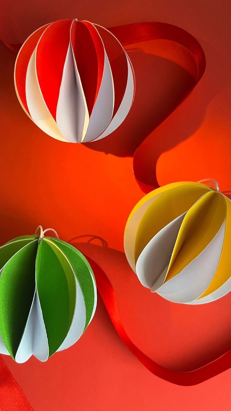 Three striped paper ornaments in red, yellow, and green on a red background.