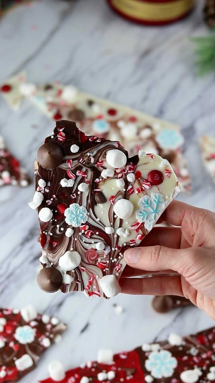 Peppermint bark with dark and white chocolate, marshmallows, and snowflake sprinkles held by hand.