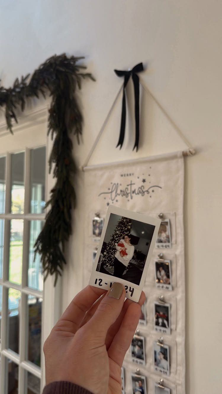 Hand holding a polaroid photo in front of a Christmas photo wall hanging