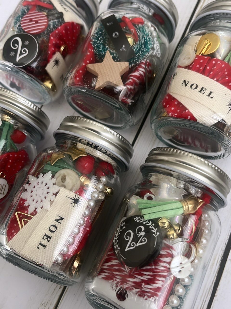 Mason jars filled with red and white Christmas craft supplies and Noel ribbons.