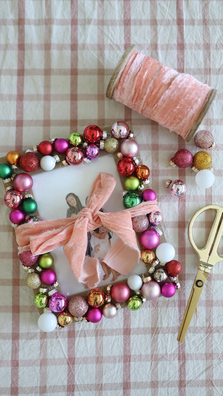 Handmade picture frame decorated with colorful Christmas ornaments and a pink velvet bow.