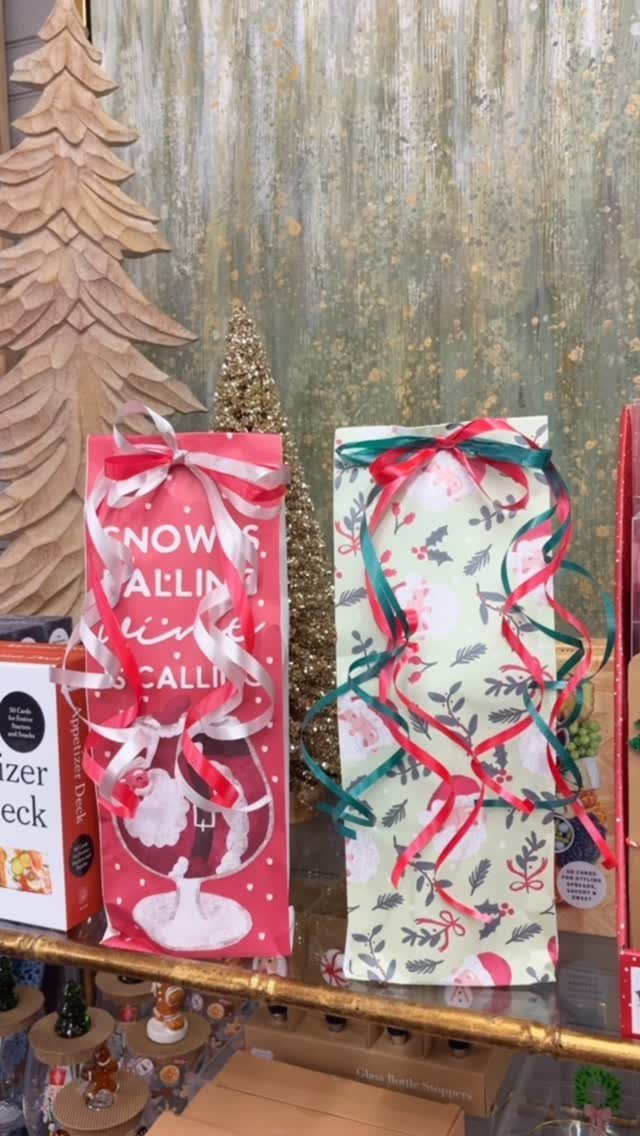 Two festive fabric wine gift bags with ribbons on a gold-trimmed shelf.