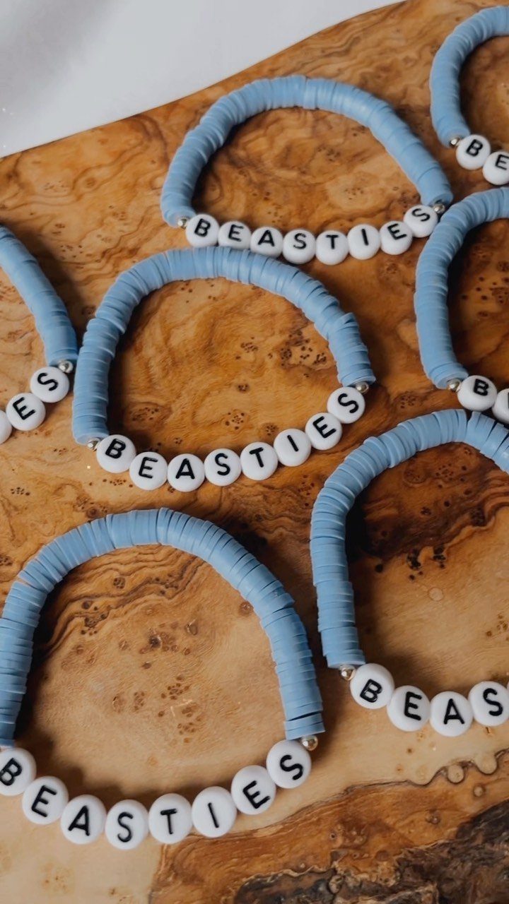 Light blue clay disc bracelets with white letter beads spelling BEASTIES on wood.