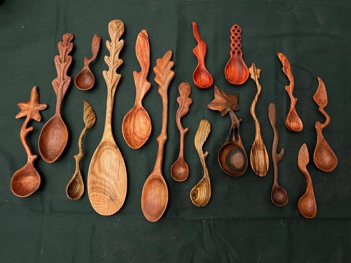 Hand-carved wooden spoons with decorative organic handles on a dark green fabric background.