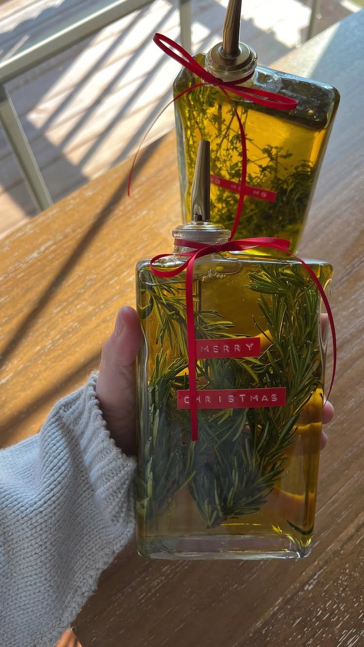 Infused olive oil bottles with rosemary sprigs and red Christmas ribbons on wood.