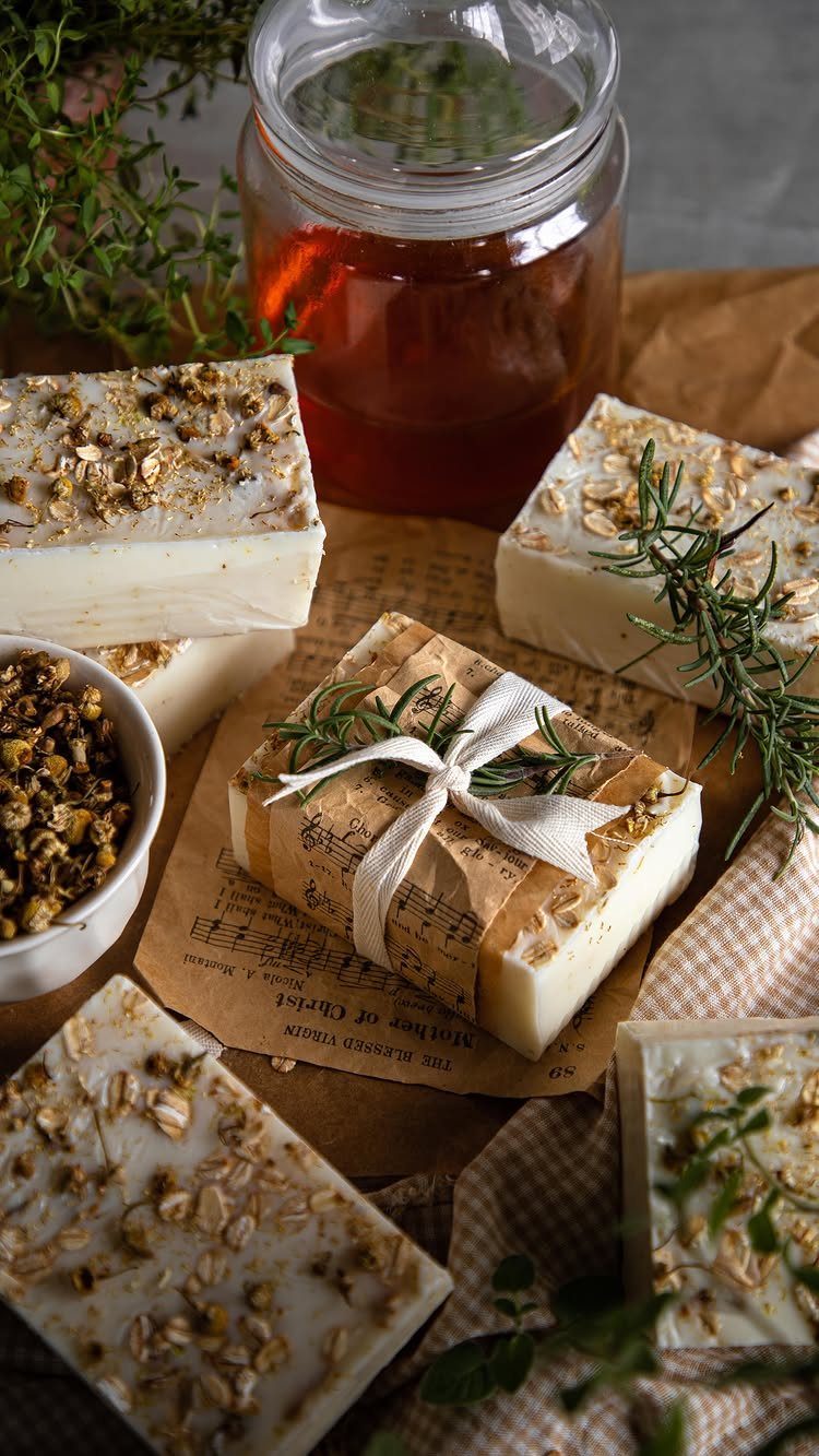 Handmade white soap bars with oats and herbs, one wrapped with a ribbon.