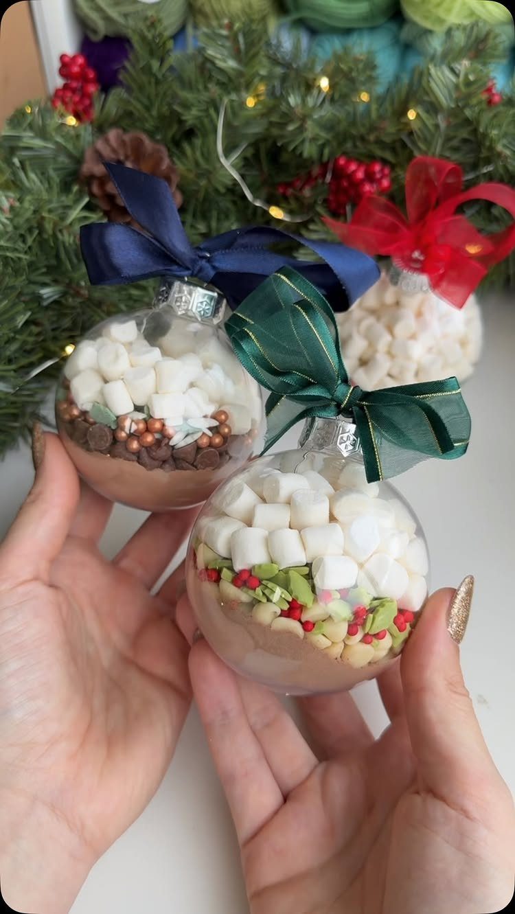 Clear Christmas baubles filled with hot cocoa mix and marshmallows held by hands.