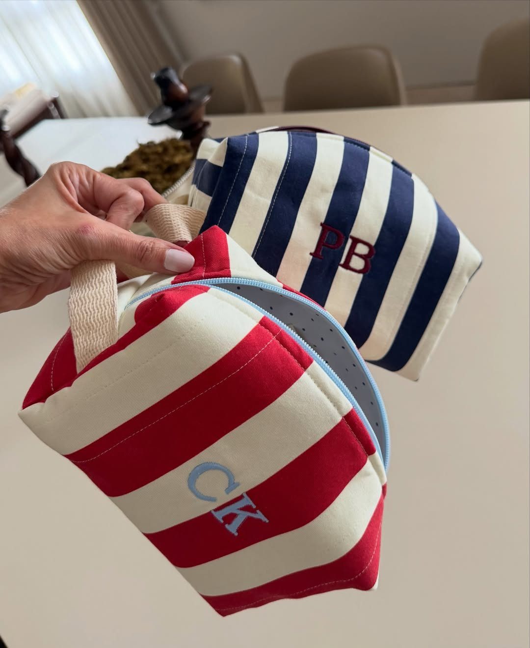 Two striped canvas pouches with monogrammed initials held over a white table.