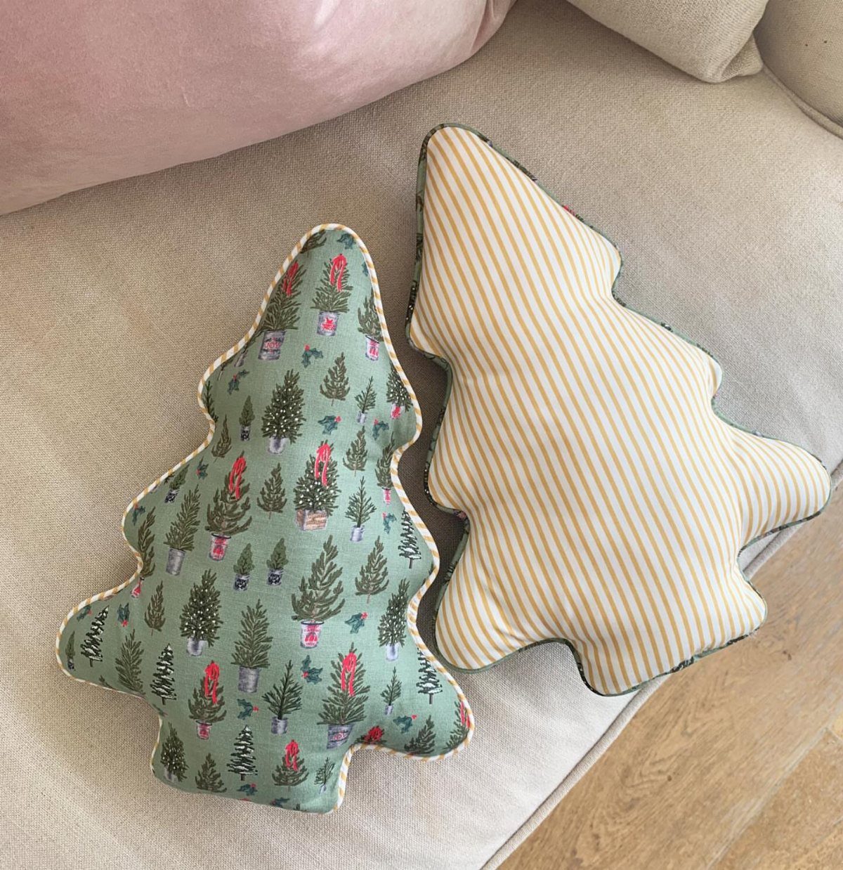 Two Christmas tree-shaped sewn pillows, one patterned and one striped, on a sofa.