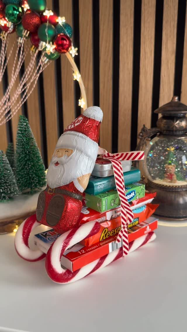 Santa figurine on a candy cane sleigh filled with chocolate bars and ribbons.