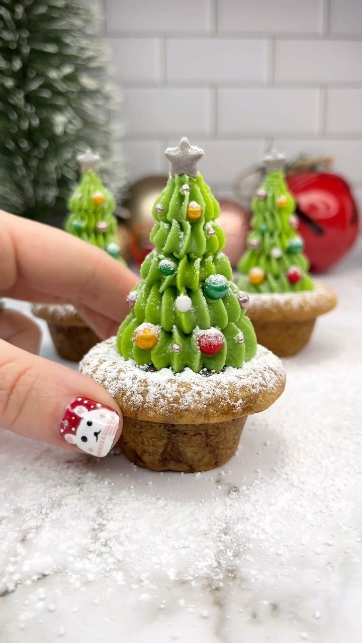 Christmas tree cupcake with green frosting and sprinkles held by a hand.